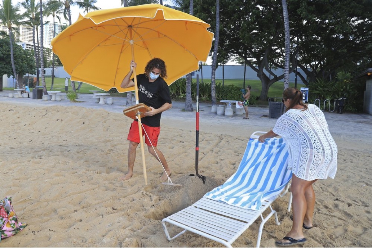 Mitch Kemp (trái) đang xếp ghế cho khách tại bãi biển Waikiki, Hawaii. Công ty khai thác bãi biển này chỉ vừa mở trở lại hôm 15/10, sau khi đóng cửa từ tháng 3/2020. Bà Leena Kilman (phải) là vị khách đầu tiên của công ty sau khi hoạt động lại.