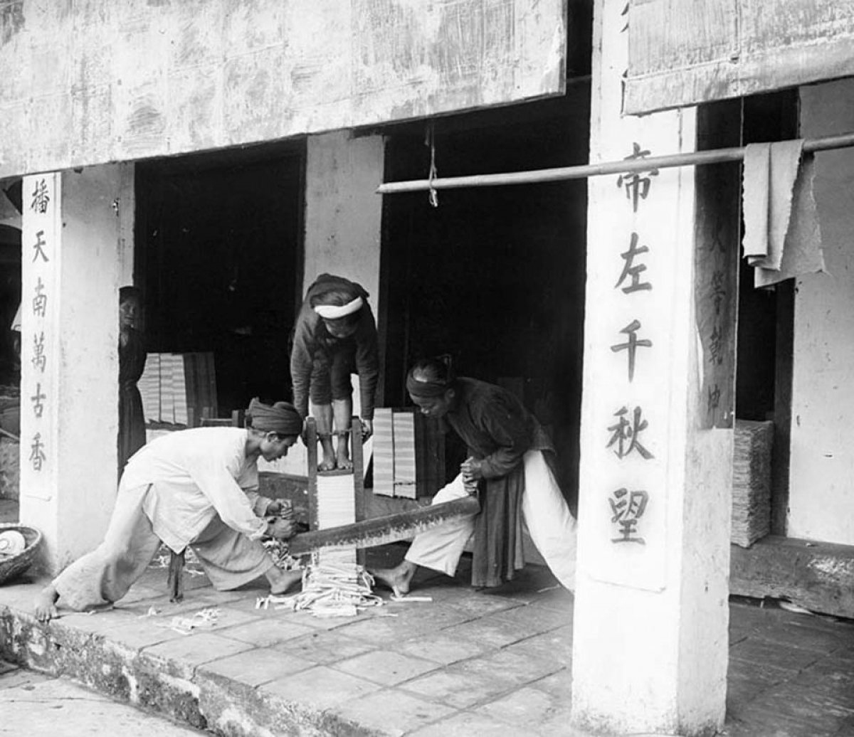 Cảnh xén đóng sách trong đền Ngọc Sơn. Một phụ nữ ép chồng sách xuống và hai nam giới xén các trang giấy.
 