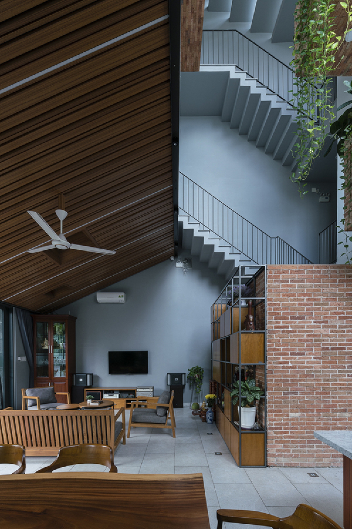 Phía trên phòng khách là một trần gỗ dốc gợi nhắc mái nhà dân gian. Chất liệu gỗ và gạch trần gợi cảm giác gần gũi, ấm áp.