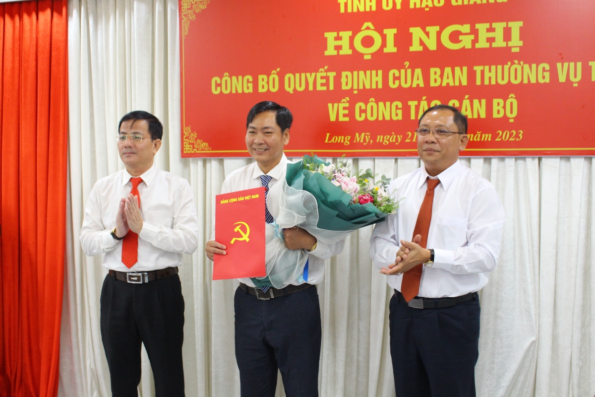 Ông Trần Văn Huyến - Phó Bí thư Thường trực Tỉnh ủy, Chủ tịch HĐND tỉnh Hậu Giang (bìa trái) và ông Trần Chí Hùng - Tỉnh ủy viên, Bí thư Huyện ủy Long Mỹ (bìa phải) trao quyết định và tặng hoa chúc mừng ông Nguyễn Vũ Trường.