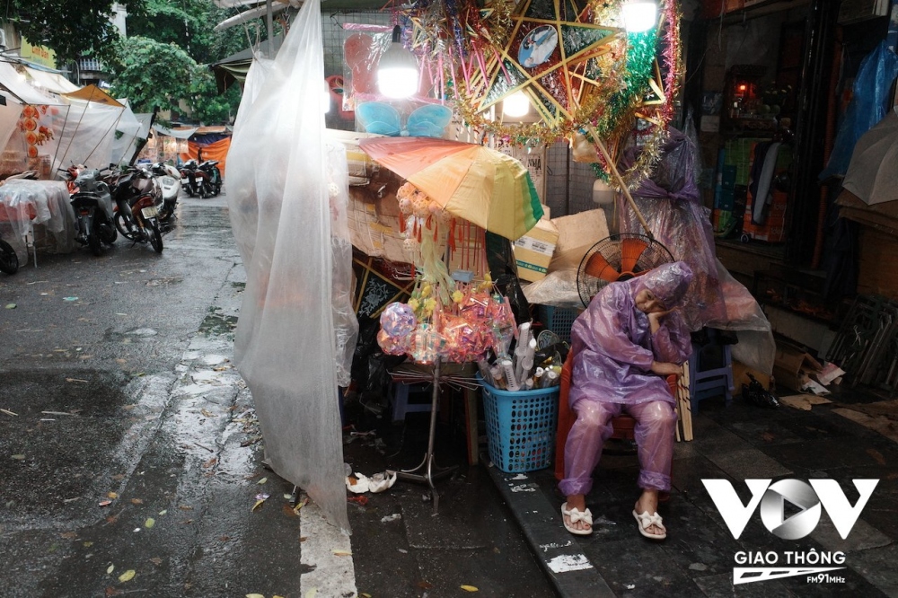 Một người bán hàng ủ rũ trong cơn mưa bên quầy hàng trên phố Hàng Mã.