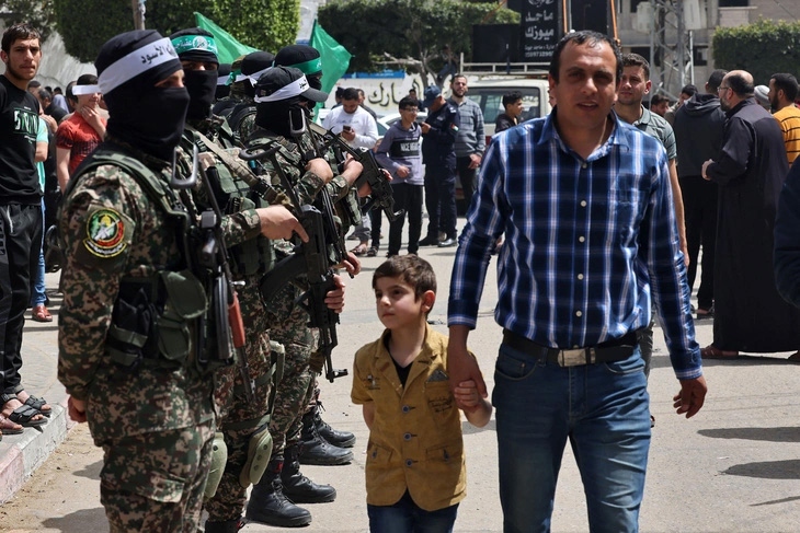 Một người đàn ông Palestine cùng con trai đi ngang qua các thành viên của Hamas ở thành phố Jabalia, phía Bắc dải Gaza, ngày 7/4. Ảnh: AFP