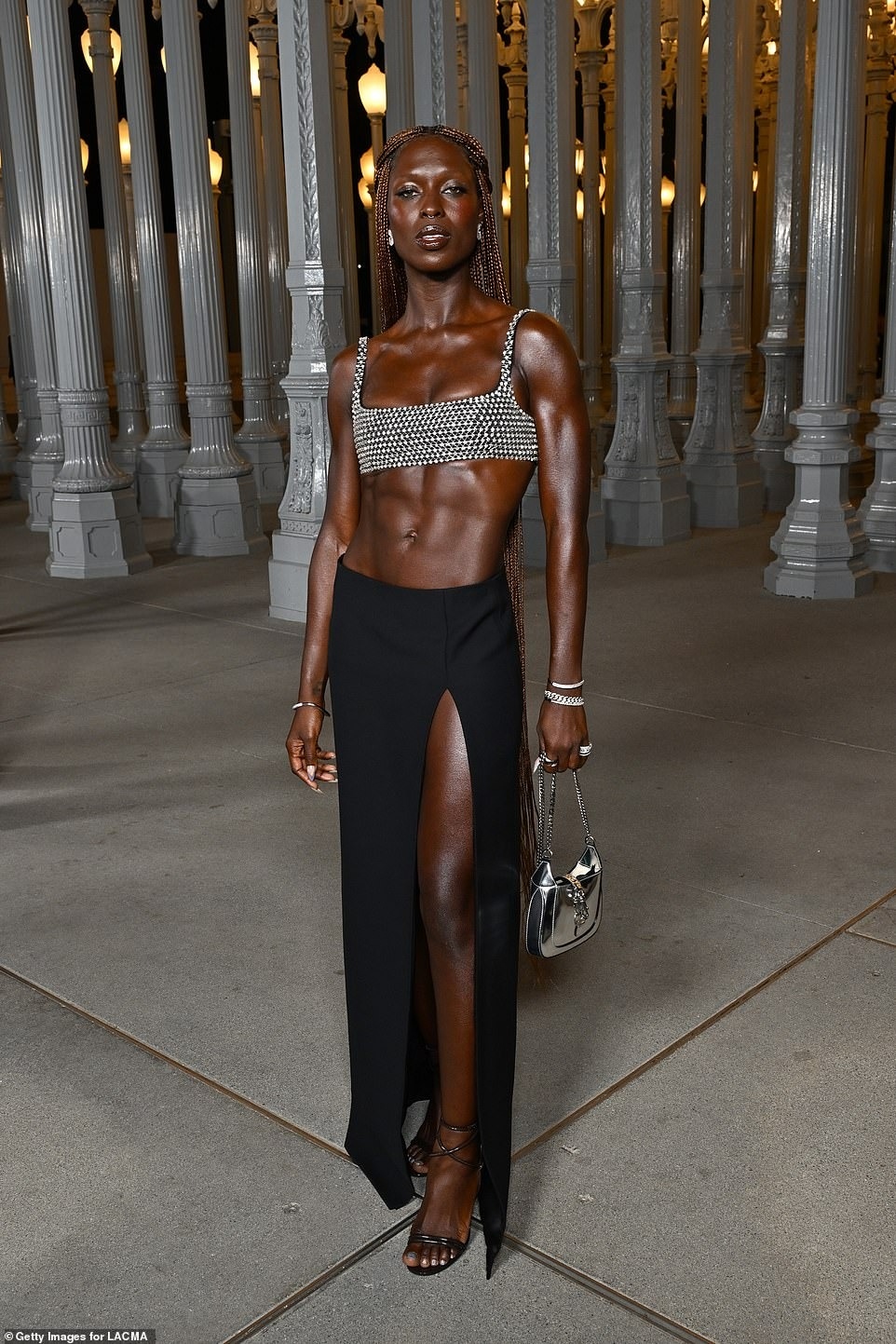 Jodie Turner-Smith khoe cơ bụng trong chiếc áo crop top màu bạc rực rỡ, kết hợp với váy maxi đen xẻ cao táo bạo.