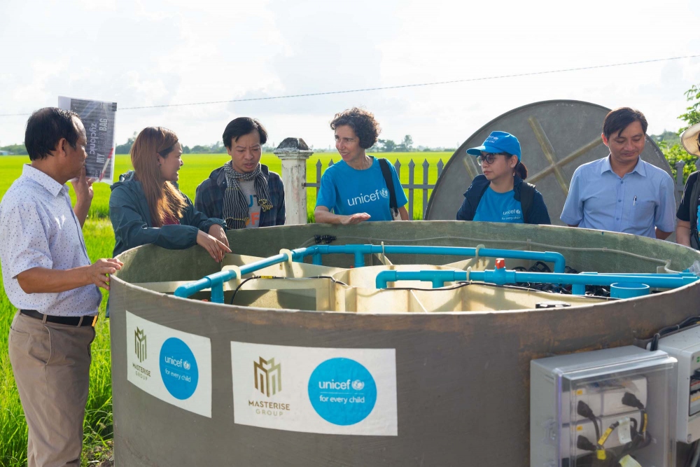 Cán bộ UNICEF và đại diện địa phương lắp đặt thiết bị của nhà vệ sinh không phát thải (trái). Học sinh trường tiểu học Long Phú C đứng trước công trình vừa được bàn giao và đi vào vận hành