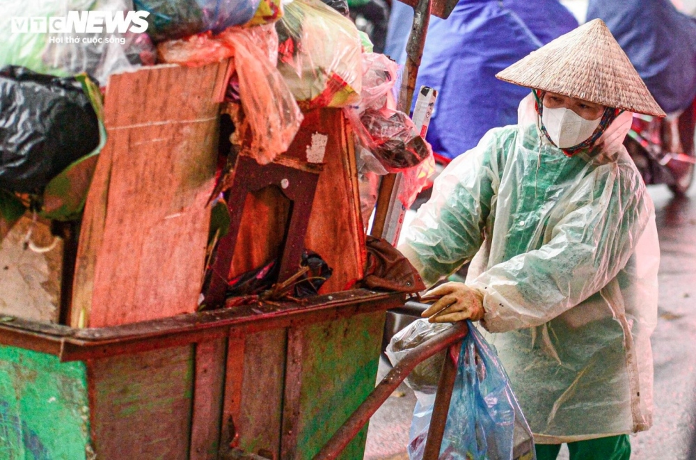 A worker wears a Non La (conical hat), face mask, gloves, and raincoat to cope with the cold spell.