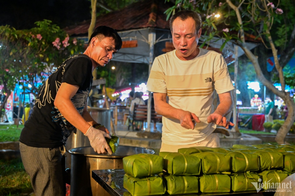 Many tourists attentively watch artisans wrap and cook banh chung (square glutinous rice cake), an indispensable dish during the Tet holiday.