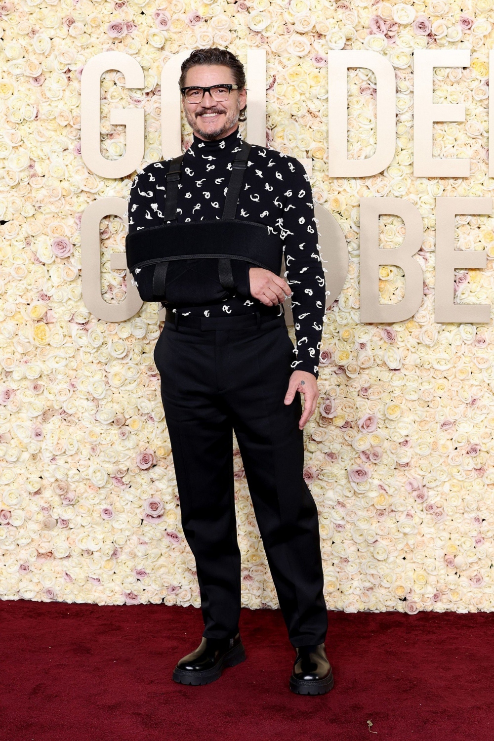 Pedro Pascal với bộ trang phục toàn màu đen của Bottega Veneta, trong đó có áo len có nút thắt chi tiết và quần len đen.