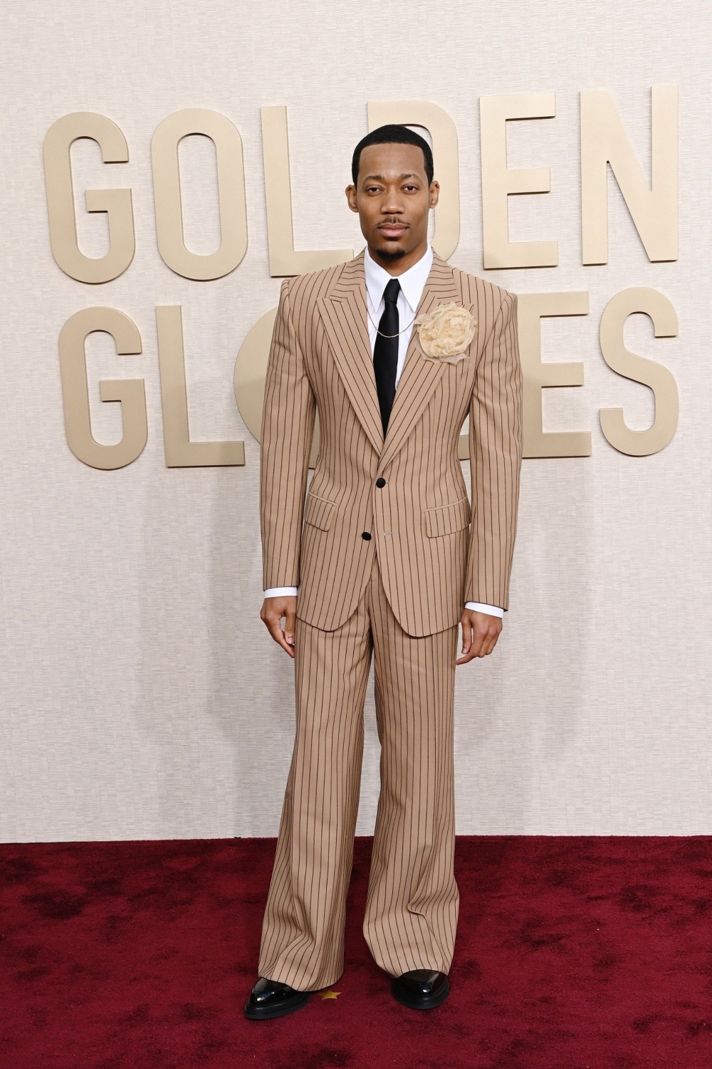 Ngôi sao của “Abbott Elementary” Tyler James Williams mặc bộ đồ Dolce &amp; Gabbana ống rộng có sọc nhỏ kết hợp với một chiếc trâm cài hình hoa hồng và vòng cổ David Yurman.