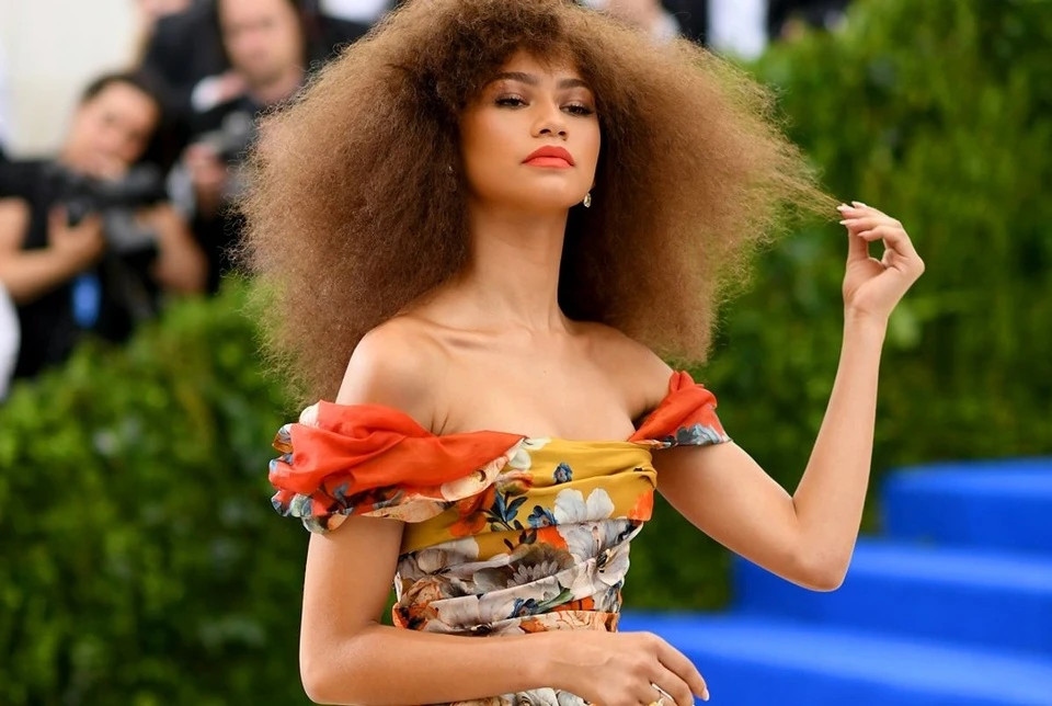 Dù bộ cánh khá lạc đề với chủ đề Met Gala 2017, khi không nói lên về tính tiên phong của nhà mốt Comme des Garons được sáng lập bởi NTK Rei Kawakubo, thì Zendaya vẫn lọt top mặc đẹp trong đêm. Được tô màu bằng các sắc thái sặc sỡ như quýt, vàng chanh và xanh lam, trang phục của nữ diễn viên là một trong những bộ đồ bắt mắt nhất chương trình. Cô tăng sức hút với chiếc nhẫn kim cương màu vàng ForeverMark và hoa tai lấp lánh.