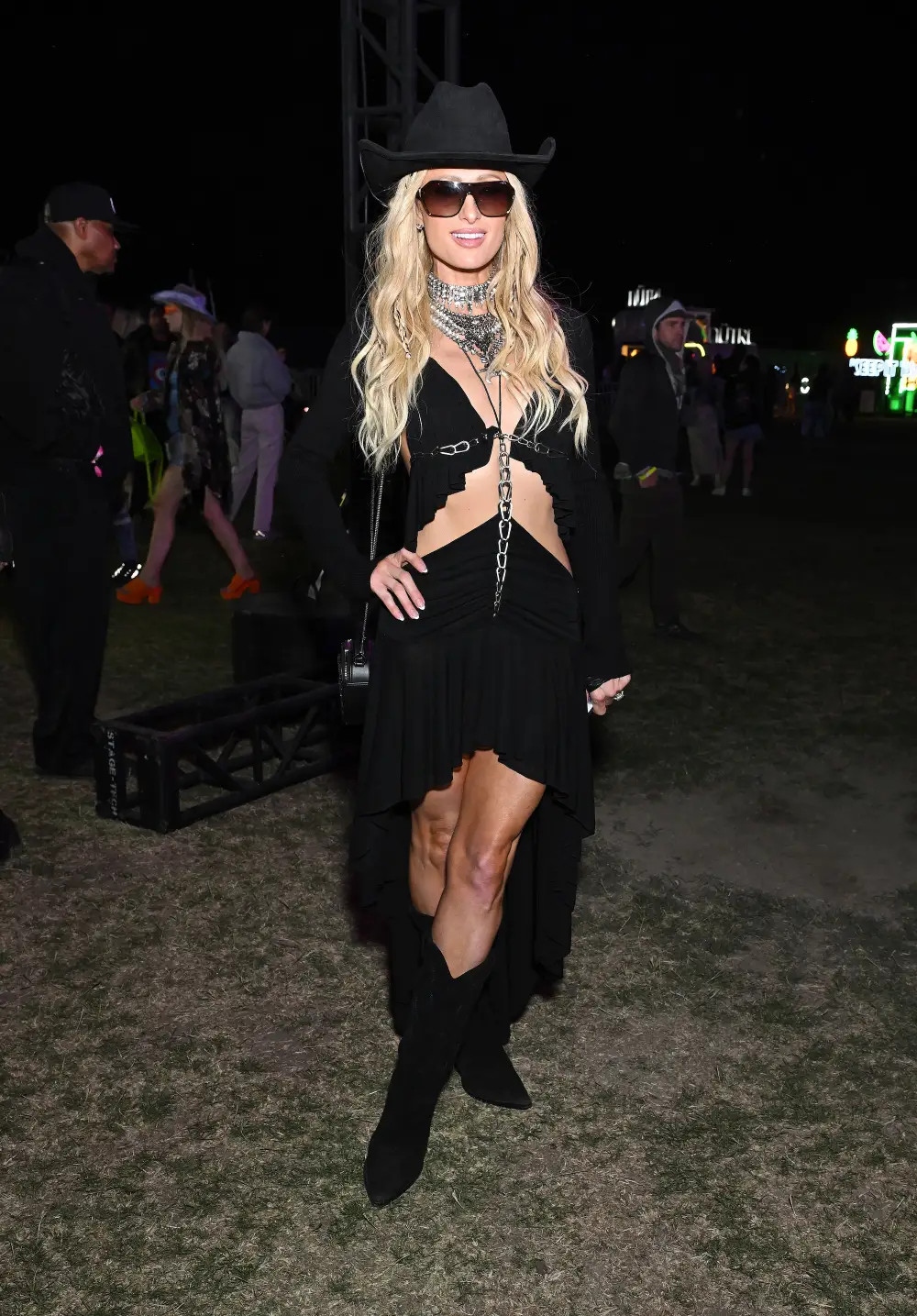 Áo crop top và váy của Paris Hilton nổi bật với những đường diềm xếp nếp, tương phản với sợi dây chuyền trang trí vạt áo. Cô phối hợp thêm vài chiếc dây chuyền bạc và một chiếc mũ cao bồi màu đen cho vẻ ngoài xinh đẹp.