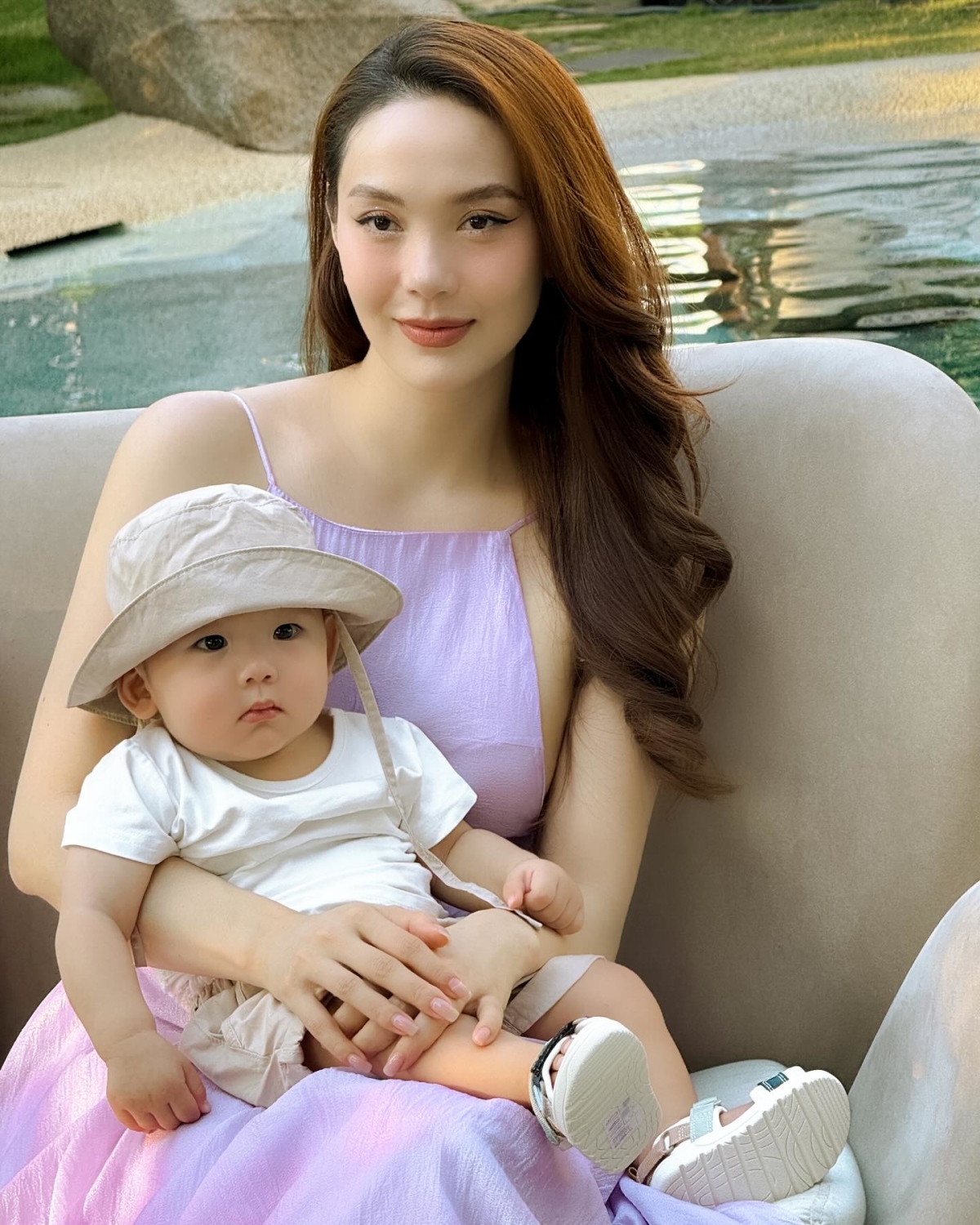 Minh Hằng bế con trai khi đi biển nghỉ dưỡng ở Phú Quý. Trong vòng tay mẹ, cậu nhóc biểu cảm phụng phịu, được nhiều khán giả khen dễ thương. Minh Hằng sắm cho con trai 8 tháng tuổi trang phục mát mẻ, phối cùng mũ tai bèo để tránh nắng.