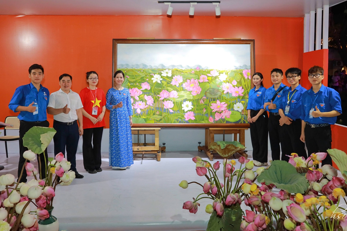 Họa sĩ Kim Đức (áo dài) bên bức tranh "Liên hoa tịnh cảnh" trưng bài tại Lễ hội Sen Hà Nội 2024