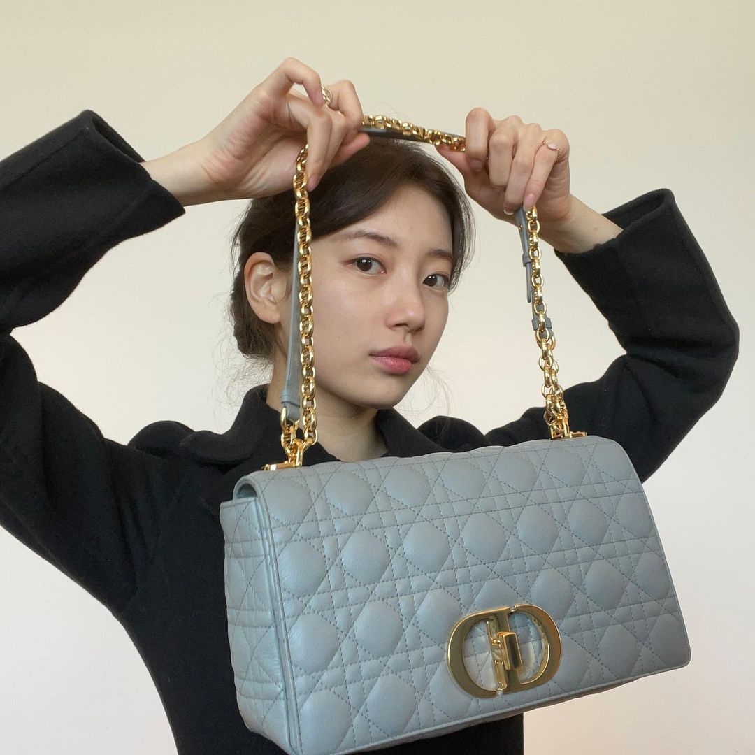 Chiếc túi Dior Caro mang đến sự nữ tính vượt thời gian. Kiểu dáng hình hộp chữ nhật sắc sảo, dễ sử dụng. Quai túi được thiết kế tỉ mỉ từng mắt xích một tạo nên sự hoàn hảo cho tổng thể. Ngoài ra, họa tiết Cannage tiêu biểu vẫn được sử dụng. Suzy sắm cho mình chiếc Medium Dior Caro màu xanh, có giá khoảng 4.700 USD.