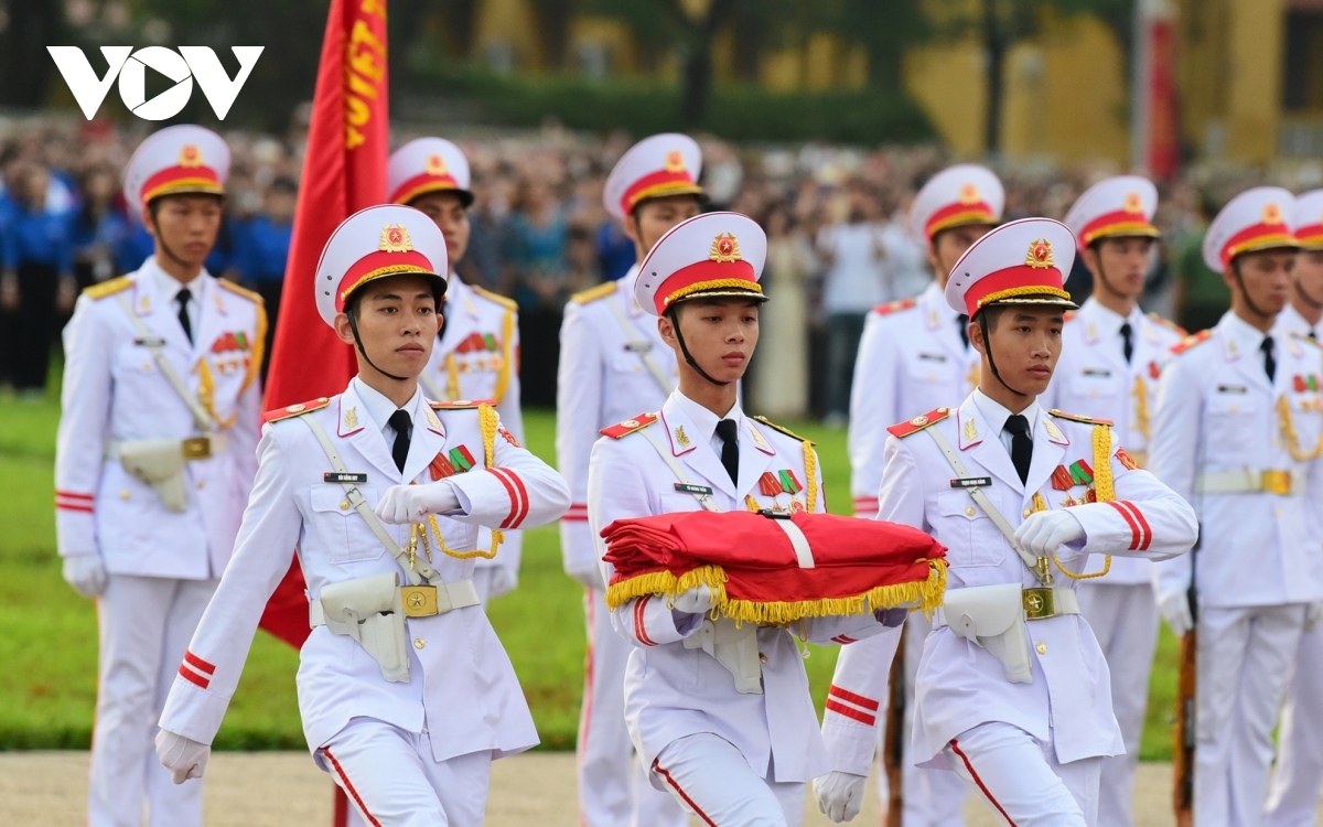 Three soldiers holding the red flag solemnly step onto a podium in preparation to undertake the main ritual.