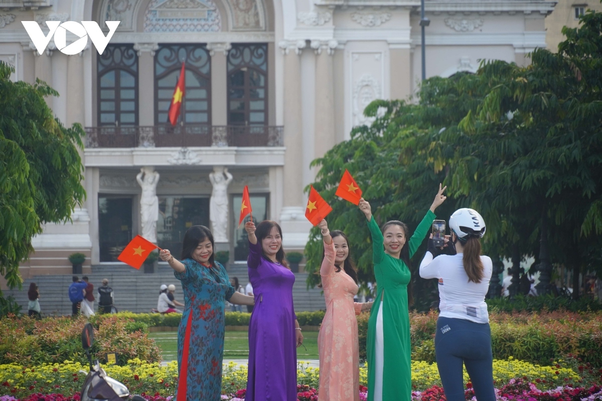 Women wearing Ao Dai and waving Vietnamese flags pose for a photo.