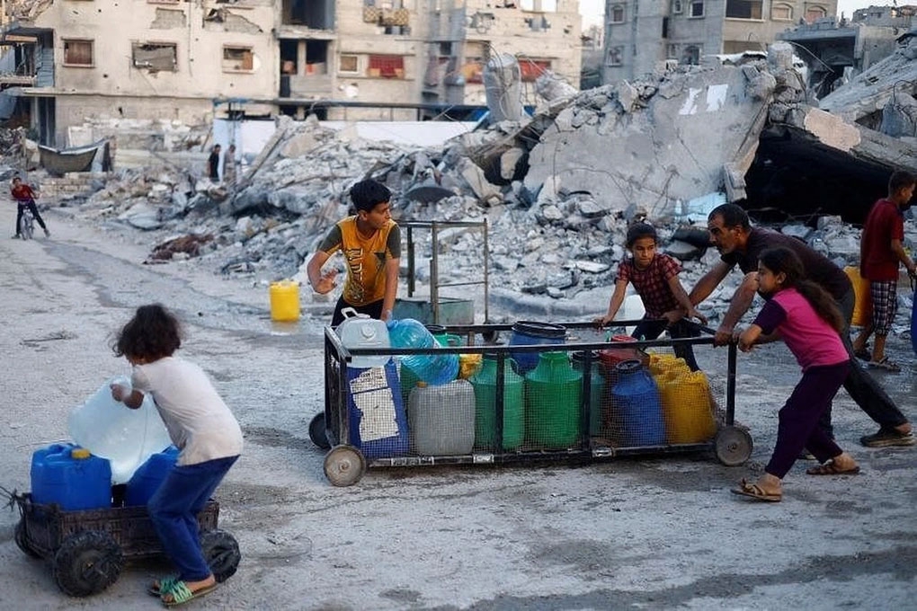 Một người đàn ông Palestine và trẻ em đẩy xe đẩy chở các thùng chứa nước ở Gaza (Ảnh: Reuters)