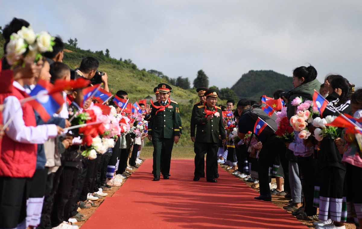 Tiếp đó, đoàn đại biểu hai nước Việt Nam và Lào đã đến thăm, tặng quà Trường Tiểu học - Trung học cơ sở Pahang. Tại đây, Đại tướng Phan Văn Giang bày tỏ xúc động khi đón nhận những bông hoa tươi thắm và chiếc khăn quàng đỏ của các em học sinh. Trong ảnh: Học sinh Trường Tiểu học - Trung học cơ sở Pahang vẫy cờ, hoa chào đón hai Bộ trưởng.