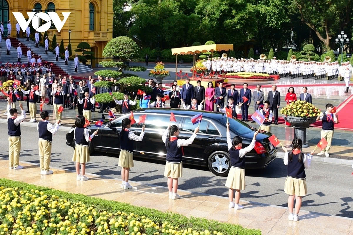 The motorcade carrying King Norodom Sihamoni of Cambodia arrives at the Presidential Palace in Hanoi, while children are present along the route waving flags of both Vietnam and Cambodia to warmly welcome the King.
