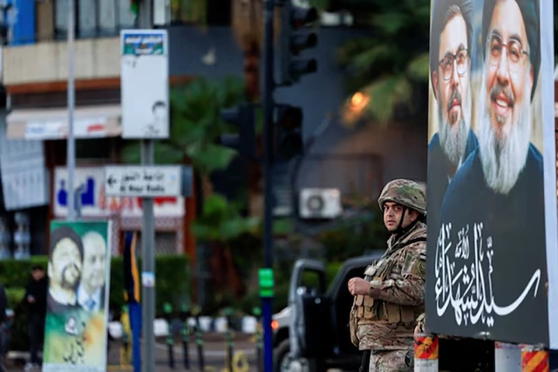 Một binh sĩ đứng gác bên cạnh tấm áp phích chân dung thủ lĩnh Hezbollah Sayyed Hassan Nasrallah và thành viên cấp cao Hashem Safieddine ở Beirut, sau khi lệnh ngừng bắn giữa Israel và Hezbollah có hiệu lực ngày 27/11. Ảnh: Reuters