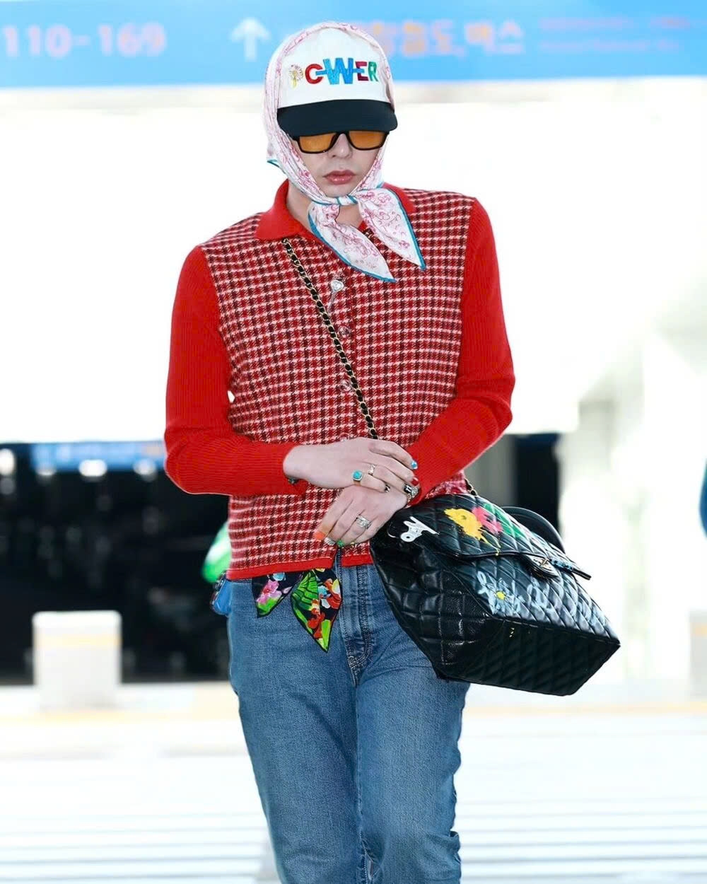 Hôm 4/11, G-Dragon được trông thấy đến sân bay Incheon (Hàn Quốc) trong một chiếc xe bán tải điện của Tesla. Vẻ ngoài nổi bật giúp nam ca sĩ thu hút sự chú ý từ giới truyền thông. G-Dragon diện áo len cài cúc màu đỏ, phối kèm quần jeans dài chấm đất. Anh đeo một chiếc túi xách Chanel chần bông được tô vẽ bắt mắt. Trưởng nhóm Big Bang đội mũ lưỡi trai, quấn khăn họa tiết theo phong cách "bà thím"