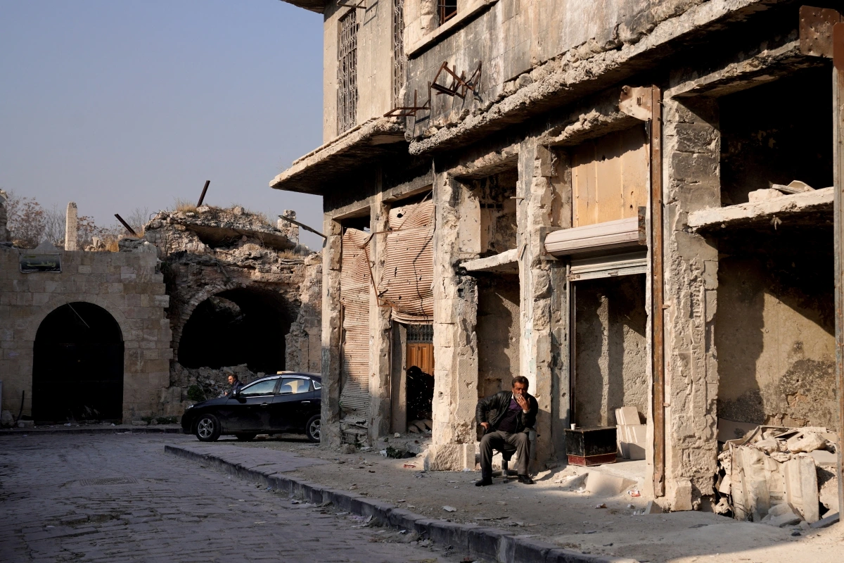 Một người đàn ông ngồi bên ngoài tòa nhà bị phá hủy ở Aleppo. Ảnh: Reuters