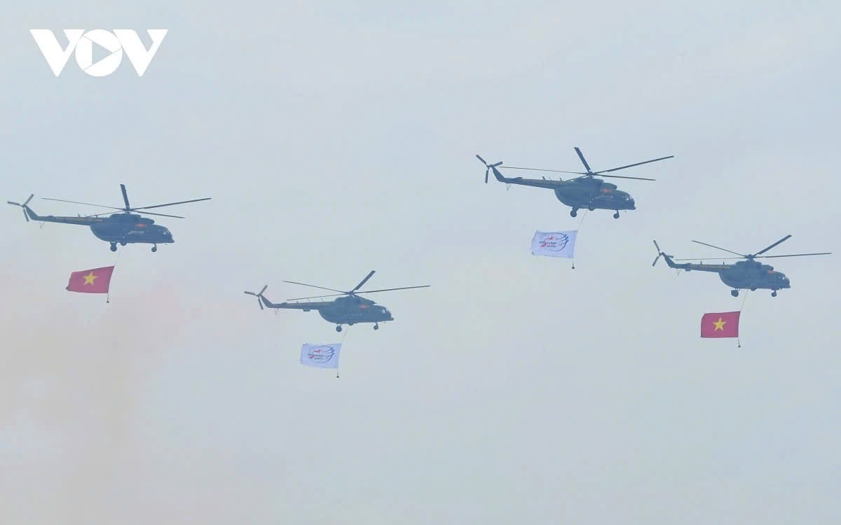 Right after the flag-raising ceremony, the Vietnam Air Force welcomes the event with a flyover of seven helicopters carrying the national flag and exhibition flag, passing over the Gia Lam airfield viewing area.