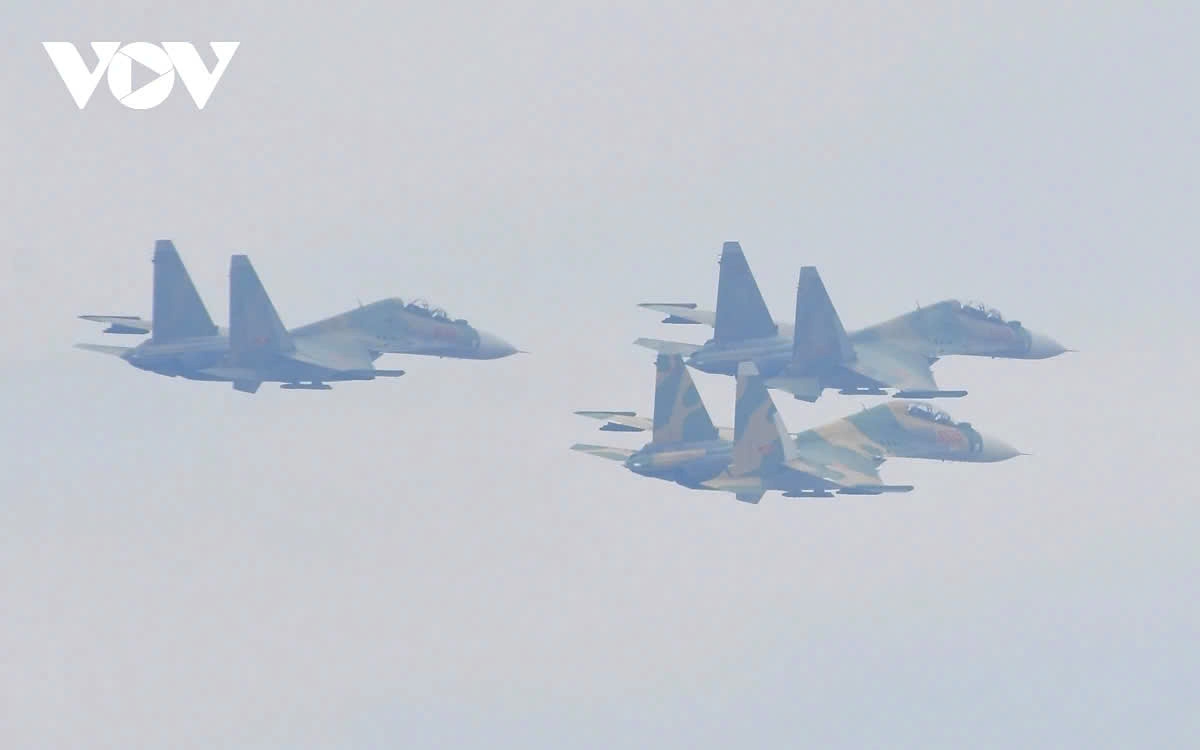 Next, 7 SU-30MK2 fighter jets fly in formation, with three in one group and four in another, passing over the ceremony stage.