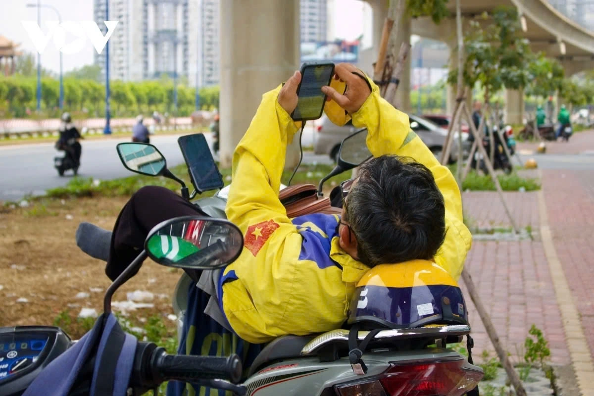“Sometimes I take rides non-stop from morning until afternoon, grabbing a quick lunch while still keeping the app on. When demand slows down, I rest under tall buildings or bridges while waiting for new orders,” says Nguyen Bao Long, a ride-hailing driver, 51.