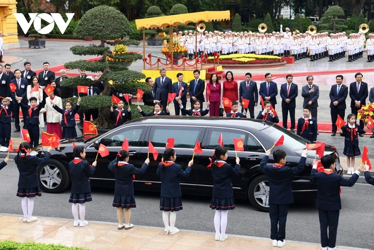 Children of Hanoi stand in two rows, waving flags to welcome the Kyrgyz Prime Minister’s motorcade as it enters the ceremonial area.