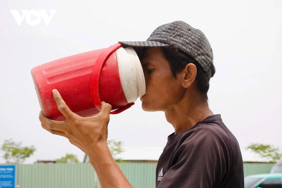 A streetlight installer in Tan Binh district shares that, despite carrying a large water bottle, he often needs to stop by residents' homes to ask for more water as the scorching sun drains his energy and dehydrates him quickly.
