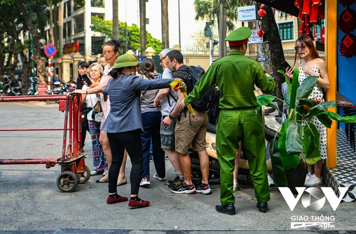 Một nhóm khách du lịch cố đi qua thanh chắn khi tàu chuẩn bị chạy qua