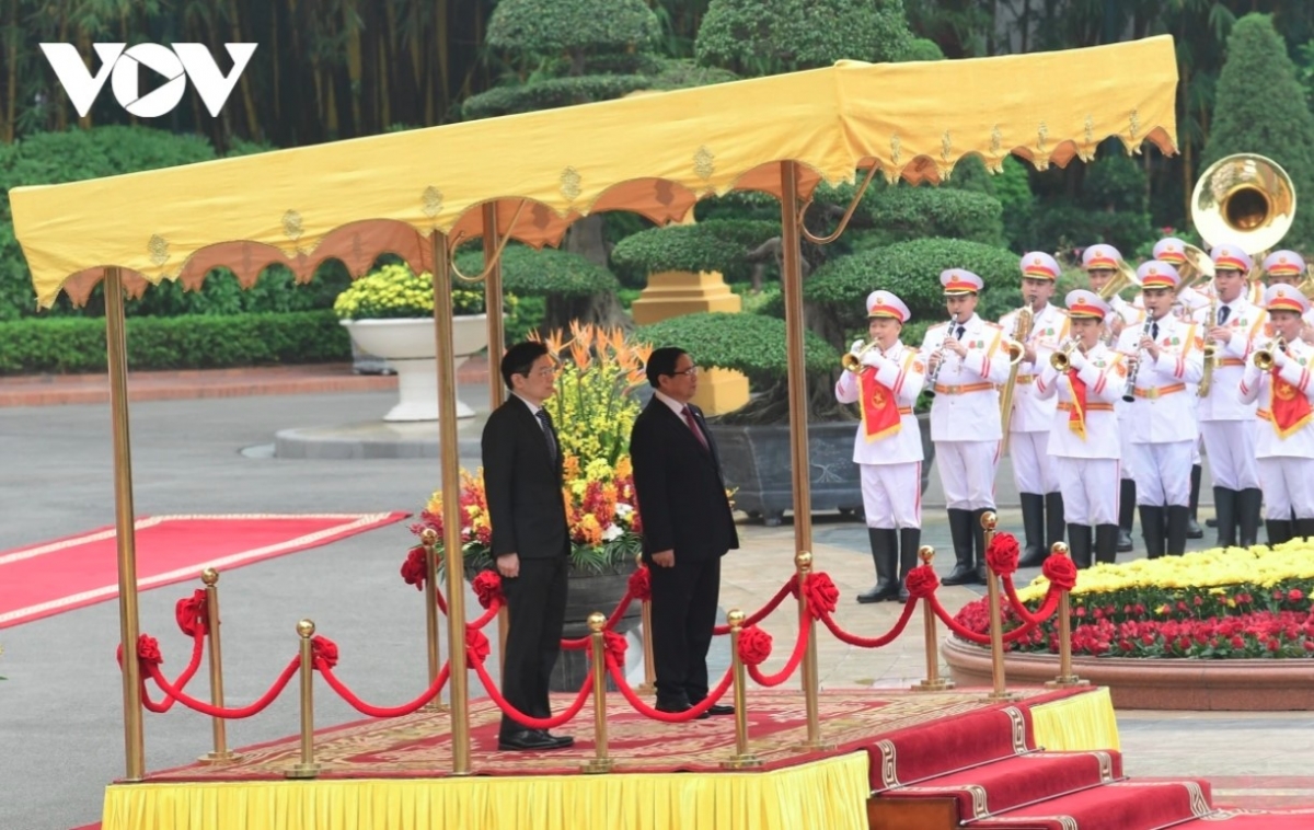 The two PMs stand on the podium while military bands play the national anthems of both nations.