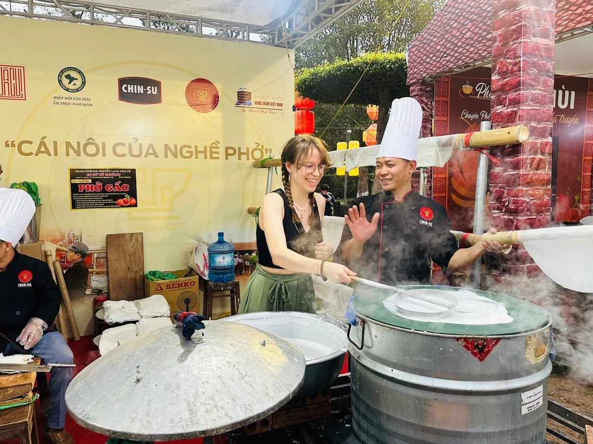 Du khách nước ngoài trải nghiệm tráng bánh phở tại gian hàng Chi hội Phở Vân Cù