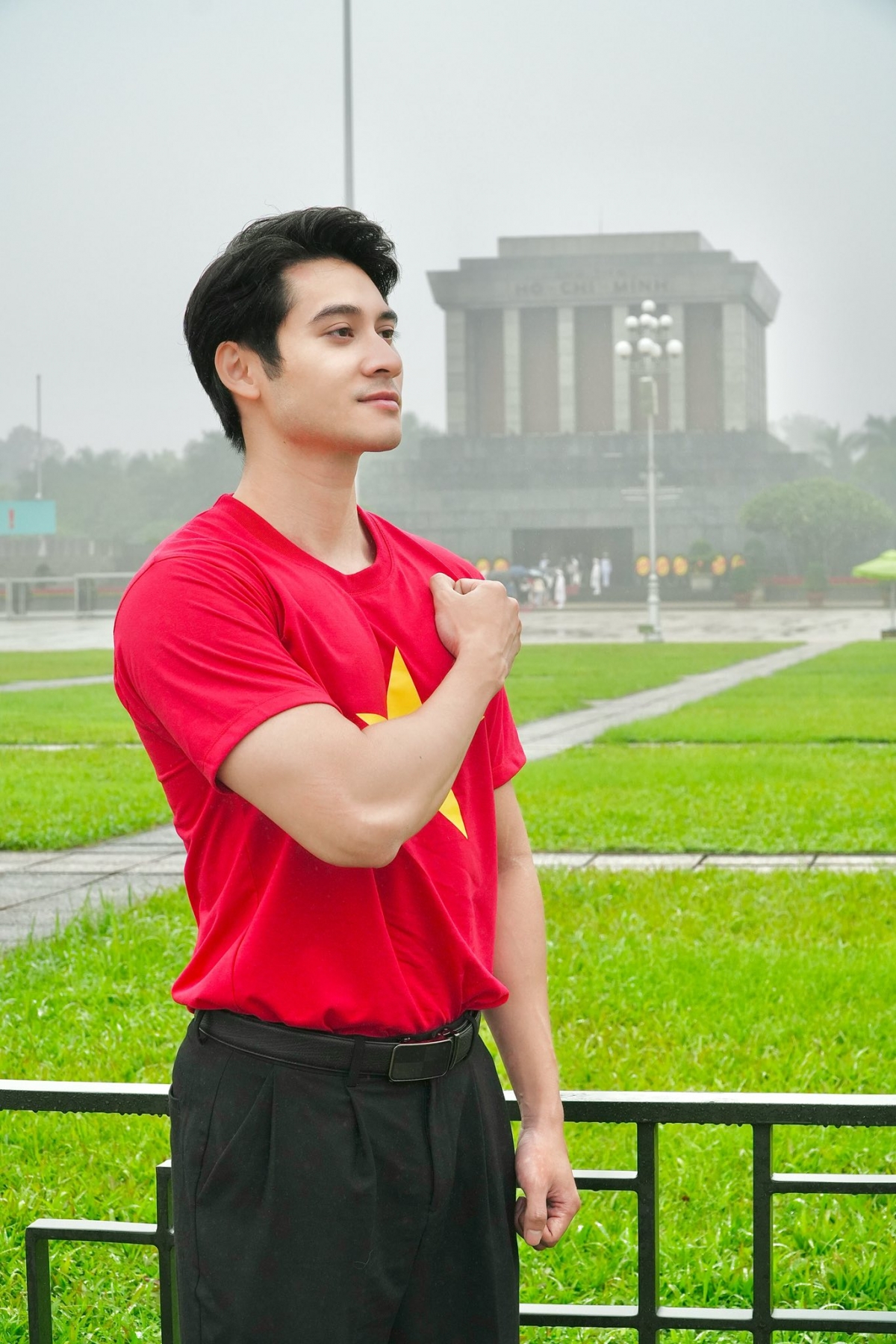 Phạm Tuấn Ngọc mặc áo cờ đỏ sao vàng chụp ảnh trước Lăng Chủ tịch Hồ Chí Minh. “Con vào thăm Lăng Bác. Mưa ướt vai mà lòng con ấm lạ”, anh viết. (Nguồn: FBNV)