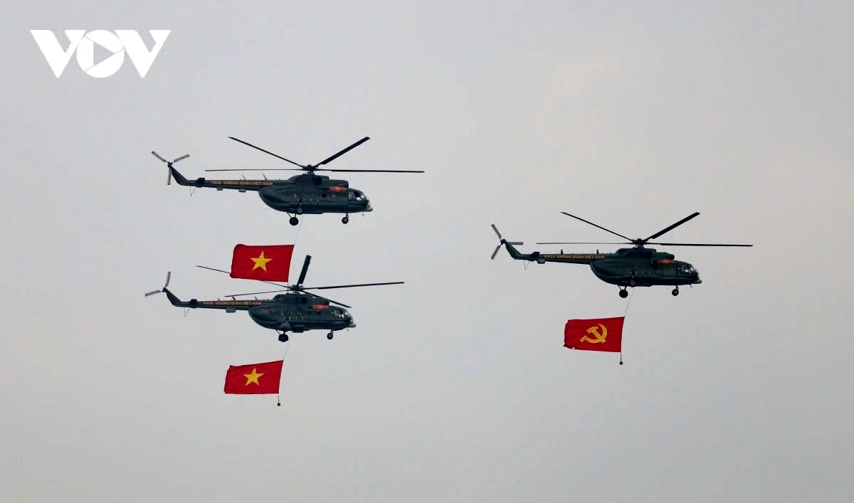 Ten helicopters fly in distinct formations past the grandstand, carrying the Party and National flags.