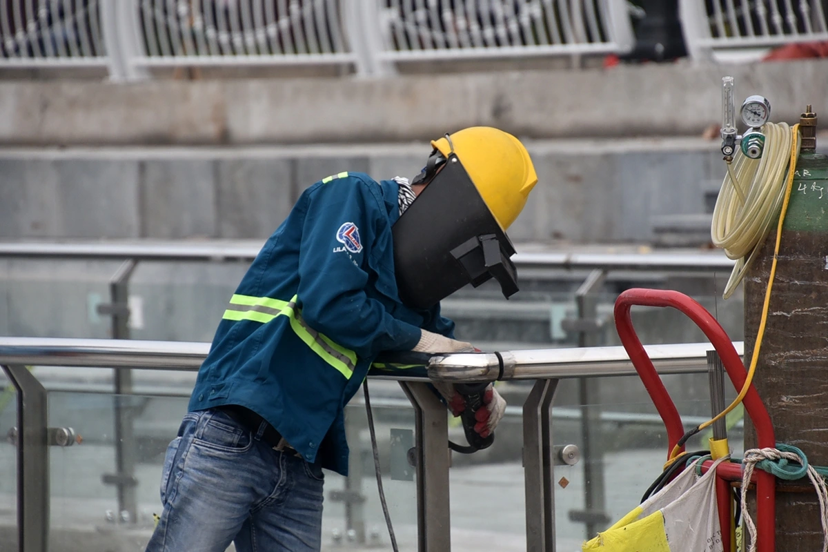 Công nhân thực hiện hàn đánh bóng lan can inox lắp kính.