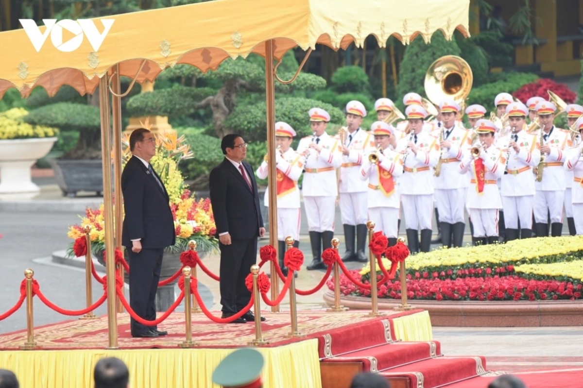 The two PMs stand on the podium while military bands play the national anthems of both nations.