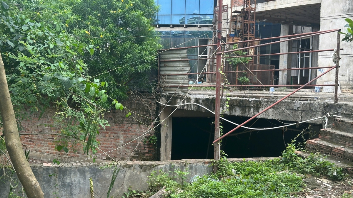 Cửa tầng hầm rỉ sét, bong tróc lớp sơn, nhiều chỗ bê tông bị nứt vỡ, lộ cốt thép hoen rỉ. Một số tấm tôn chắn tạm thời cong vênh, bị gió thổi bật ra, tạo cảm giác bỏ hoang lâu ngày.