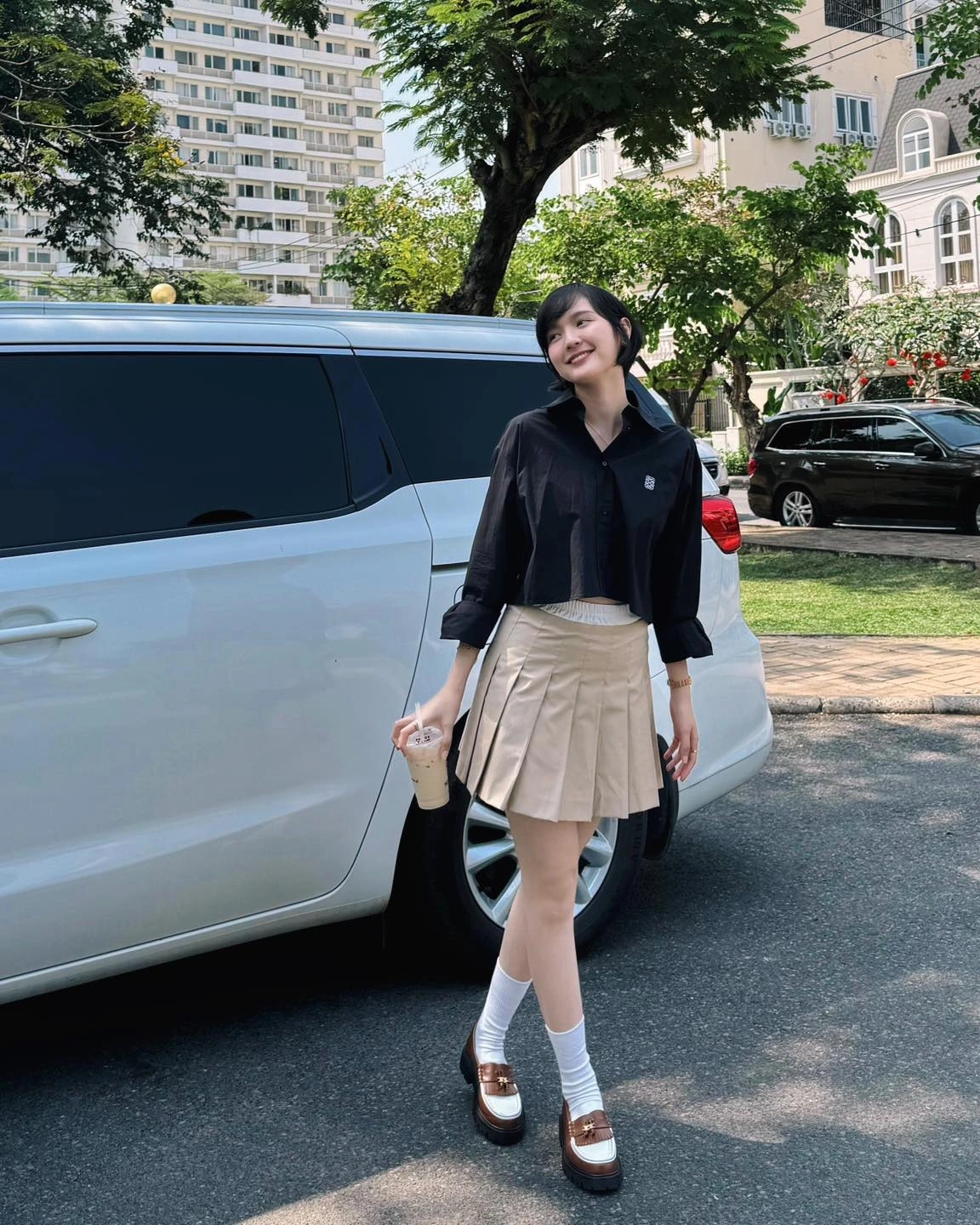 Phong cách thời trang của Hải Tú tạo dấu ấn mạnh mẽ không phải bằng sự cầu kỳ, đắt tiền mà bằng sự tối giản. Cô diện áo sơ mi dáng ngắn, phom rộng nhẹ, kết hợp cùng chân váy xếp ly và giày loafer.