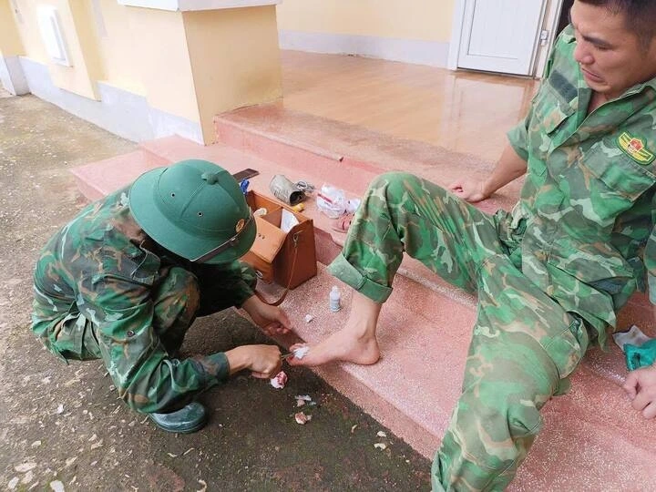 Dẫm phải đinh gỉ khi dọn nhà dân, người lính trẻ được đồng đội băng tạm vết thương rồi nhanh chóng tiếp tục công việc.