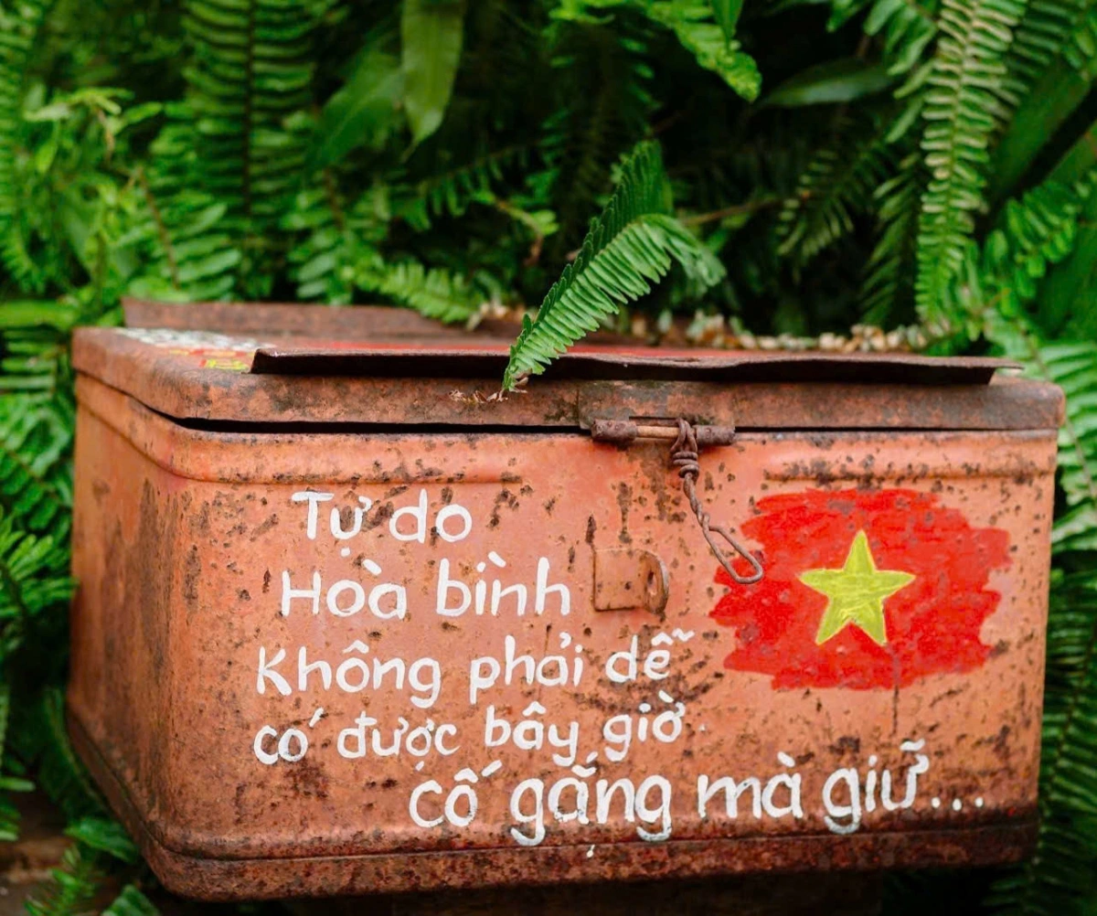 Một chiếc rương cũ từ thời bao cấp, đựng quần áo, giấy tờ và tem phiếu, được đặt bên lối đi, nhắc nhở về sự quý giá của hoà bình và thịnh vượng hôm nay.