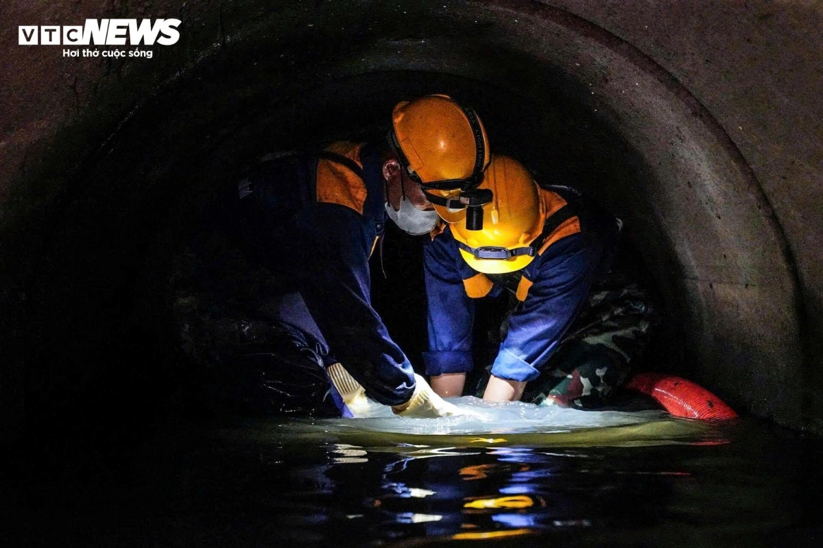 Hai công nhân cùng nhau làm việc, tay dò dẫm trong bùn đen để tìm và phá những khối tắc nghẽn, sau đó đưa ống dẫn tới khu vực đó để hút lên xe. Tình đồng đội là sức mạnh giúp họ vượt qua môi trường khắc nghiệt.