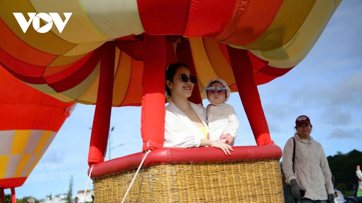 A tourist delights in taking photos with her child aboard a hot air balloon, capturing memorable autumn moments in Da Lat.