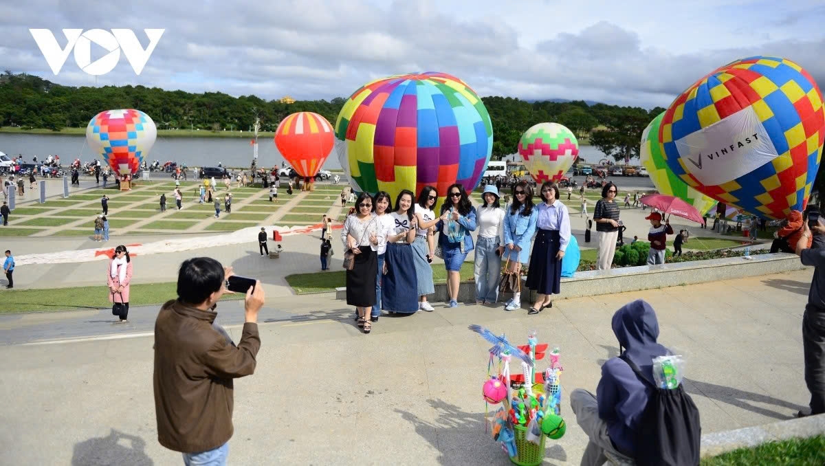 A group of tourists pose for check-in photos next to colourful hot air balloons.
