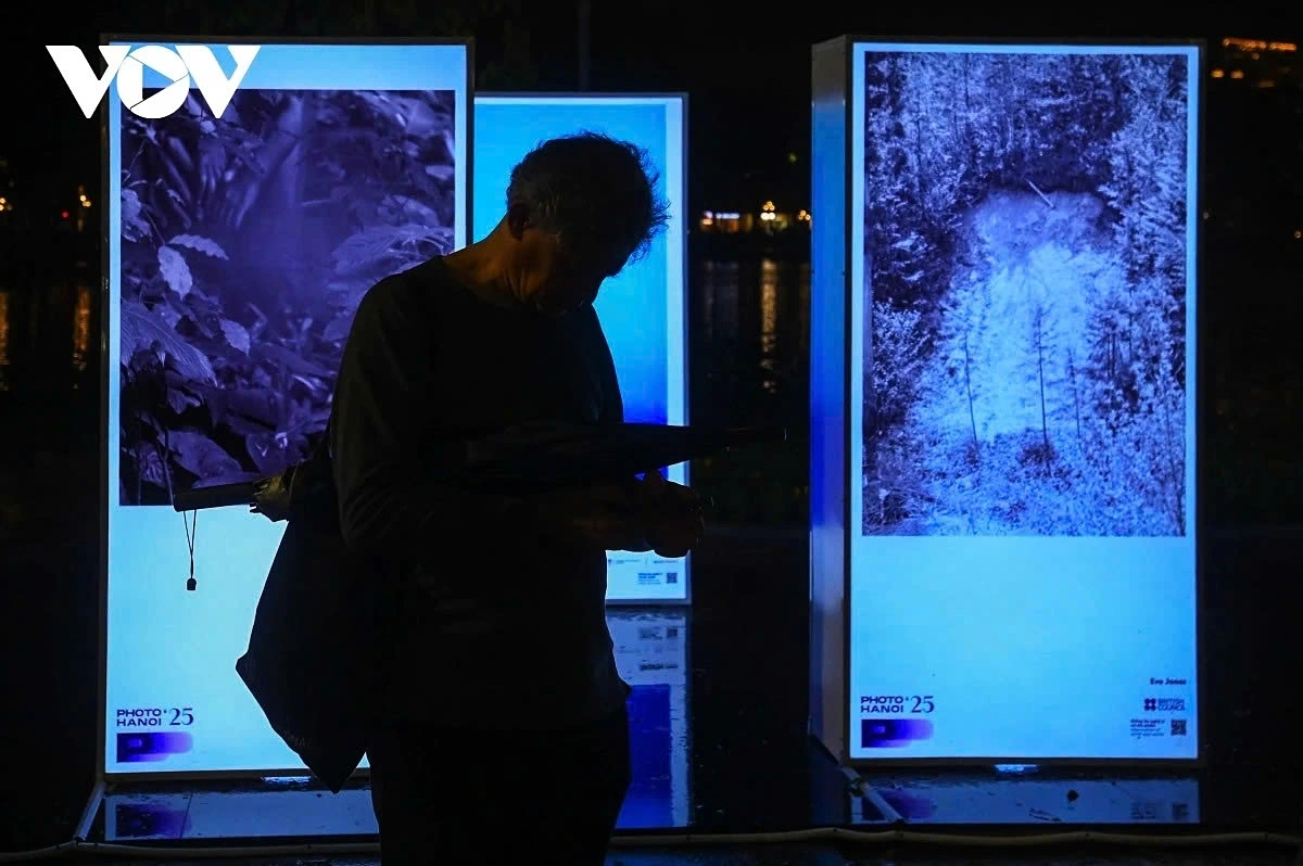 The exhibition uses illuminated vertical light boxes that reflect on the lake’s surface, creating a luminous corridor that merges art with the cityscape.